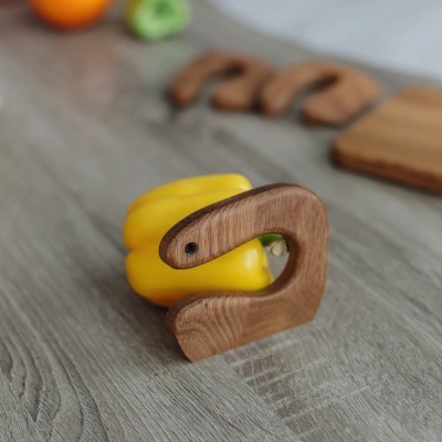 Porta-pimentos em madeira com formato de cobra, segurando um pimento amarelo, sobre superfície cinzenta de madeira.