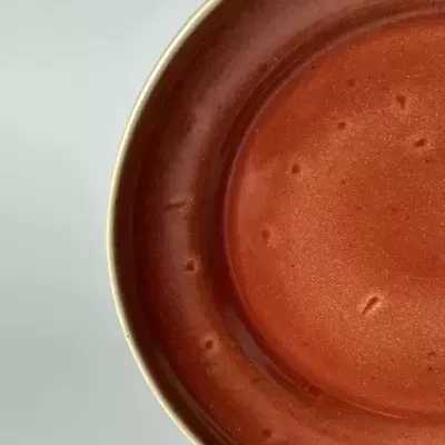 Prato de cerâmica castanho-avermelhado com borda bege e textura irregular.