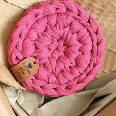 Cesto redondo de tecido cor-de-rosa trançado com etiqueta e embalagem de papel castanho em caixa.
