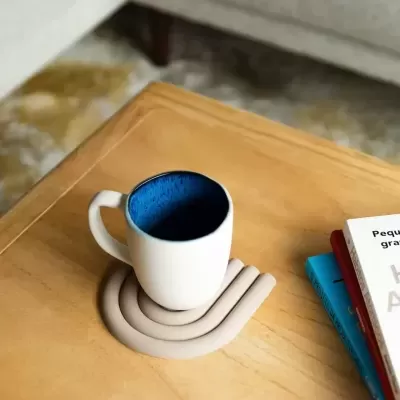 Caneca branca com interior azul num suporte bege curvo sobre mesa de madeira.
