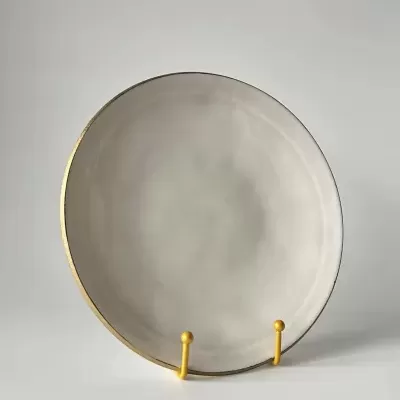 Prato redondo de cerâmica cinzento claro com borda dourada em suporte amarelo.