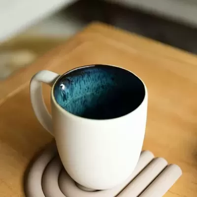 Caneca branca com interior azul escuro texturizado em cima de base em silicone cinza clara