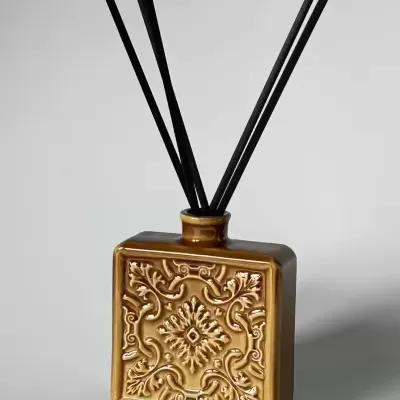 Frasco cerâmico castanho com decoração em relevo e varetas pretas de difusor de aroma.