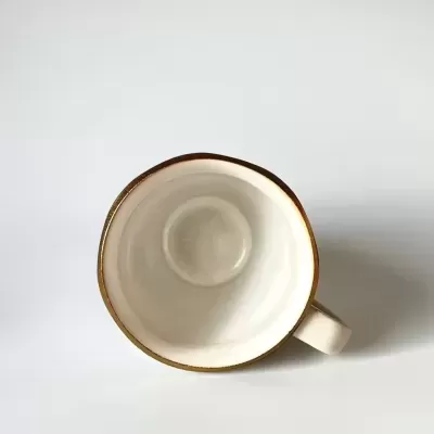 Chávena de cerâmica creme com borda castanha vista de cima.