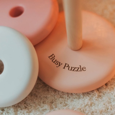 Peças redondas de madeira em tons pastel como parte de um brinquedo empilhável com inscrição Busy Puzzle