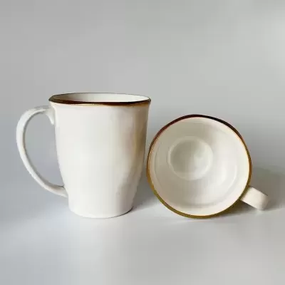 Duas canecas de cerâmica branca com bordas douradas numa superfície branca.