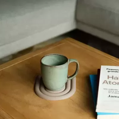 Caneca verde de cerâmica sobre suporte castanho claro numa mesa de madeira com livros ao lado