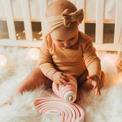 Bebé a brincar com brinquedo de madeira em forma de arco-íris rosa e branco