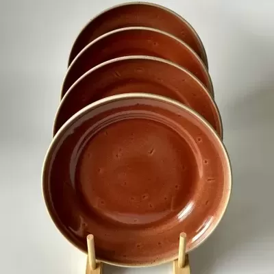 Quatro pratos cerâmicos castanhos com borda bege em suporte de madeira