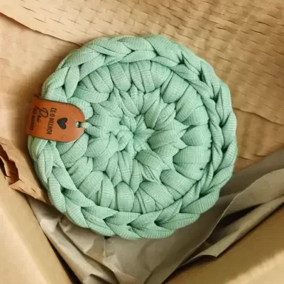 Prato raso redondo verde água tecido, com etiqueta em pele e embalagem de papel kraft.