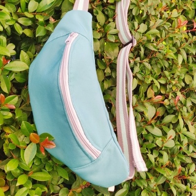 Bolsa pochete azul clara com fecho rosa pendurada em arbusto verde