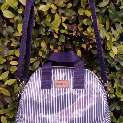 Mala riscada azul e branca com alças e tiracolo azuis pendurada em folhagem verde