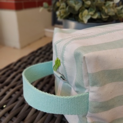 Mala pequena riscada verde e branca com pega verde claro sobre mesa de vime