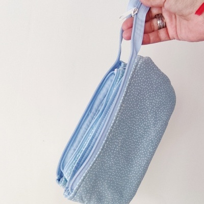 Bolsa azul claro com padrão de pontos brancos e fecho, segurada por mão