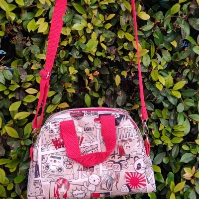 Bolsa com padrão de banda desenhada e alças vermelhas pendurada em folhagem verde