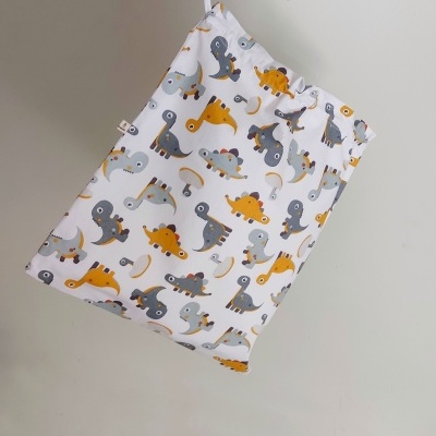 Saco de tecido branco com padrão de dinossauros coloridos pendurado na parede