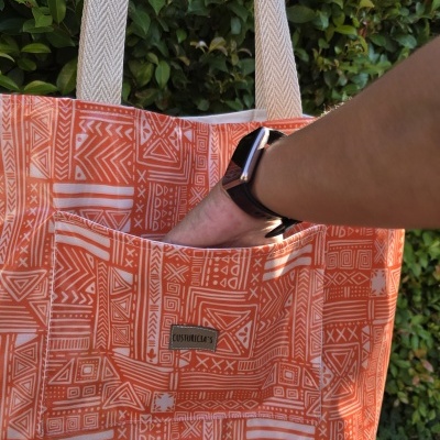 Saco de tecido laranja com padrão branco e bolso exterior com etiqueta 'COSTUREIRA'.