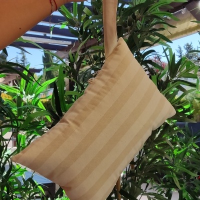 Almofada bege riscada com alça suspensa e fundo de plantas verdes