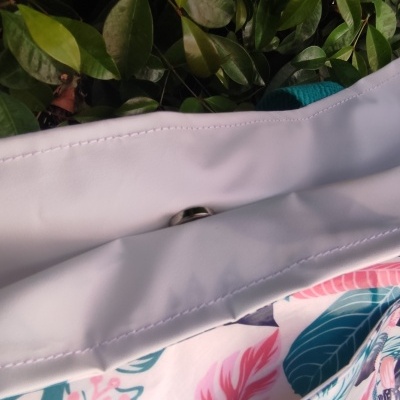 Bolsa colorida com padrão floral e botão metálico sobre folhas verdes