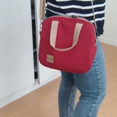 Mala pequena cor de vinho com alças bege usada por pessoa com jeans e camisola às riscas, em ambiente interior