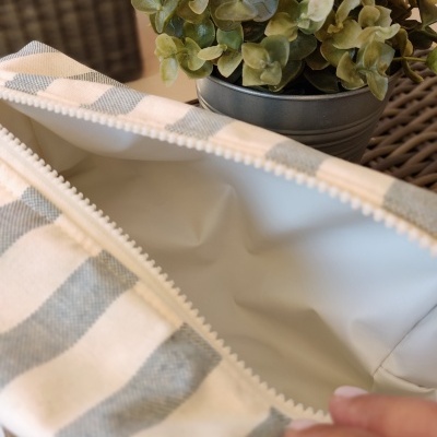 Estojo riscado cinza e branco com interior plastificado branco aberto perto de planta verde