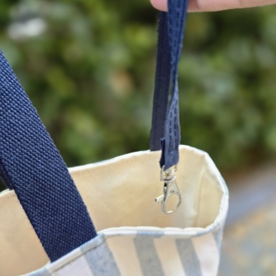 Bolsa têxtil às riscas azuis e brancas com alças azul-escuras e fecho metálico