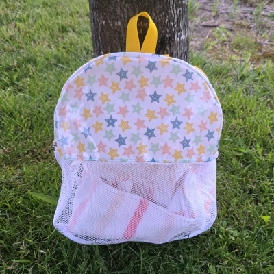 Mochila infantil padrão estrelas coloridas com bolso em rede e alça amarela pendurada num tronco de árvore