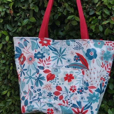 Saco tote floral azul e vermelho com alças vermelhas pendurado em árvore