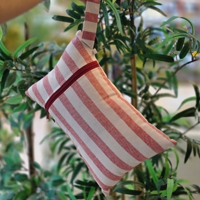 Bolsa de tecido riscada vermelha e branca com fecho vermelho e alça, pendurada junto a plantas verdes