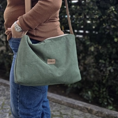 Mala verde de veludo canelado com etiqueta CUSTURICIAS usada ao ombro