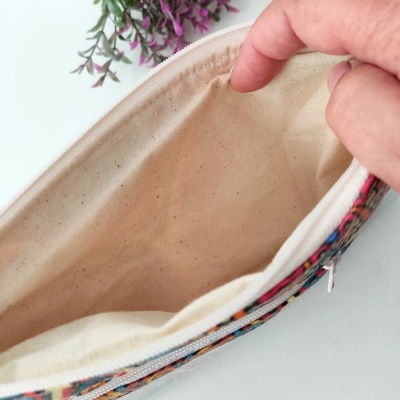 Estojo aberto em tecido colorido e interior cru com flores roxas ao lado