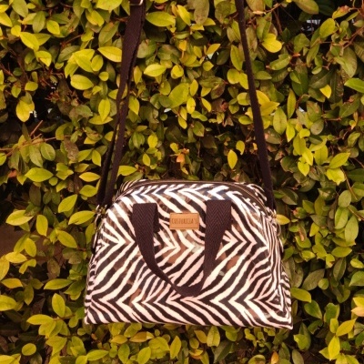 Bolsa zebrada preta e branca com alças pretas pendurada em moita verde