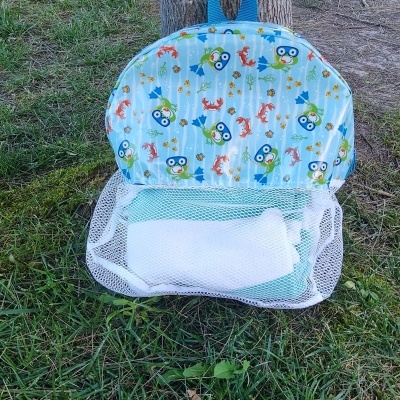 Mochila infantil azul claro com padrões coloridos e bolso de rede branco