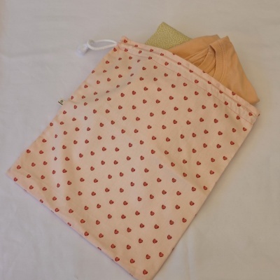 Saco tecido bege com corações vermelhos e roupa laranja e verde dentro