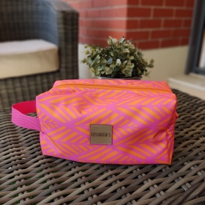 Necessaire rosa e laranja com padrão geométrico sobre mesa de vime marrom