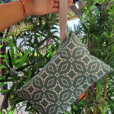 Bolsa pequena em tecido verde com padrão geométrico branco suspensa por uma mão