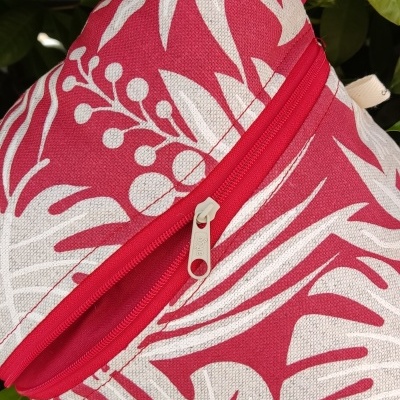 Mala rosa com padrão floral branco e fecho vermelho pendurada em planta verde