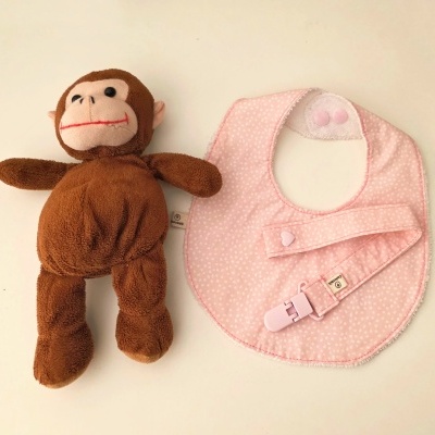 Boneco de macaco de pelúcia castanho e babete rosa com padrão de pontos brancos