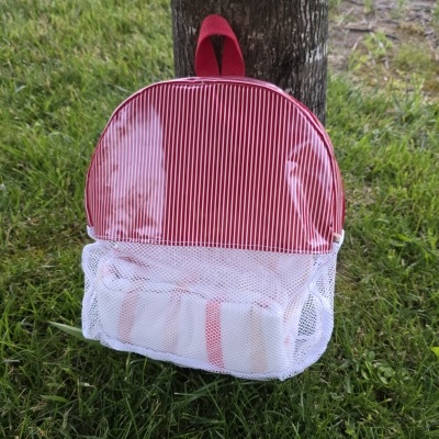Mochila infantil com riscas vermelhas e brancas e bolso em rede pendurada numa árvore