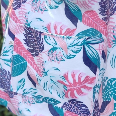 Saco de tecido com padrão floral colorido e alças azuis suspenso em frente a folhas verdes