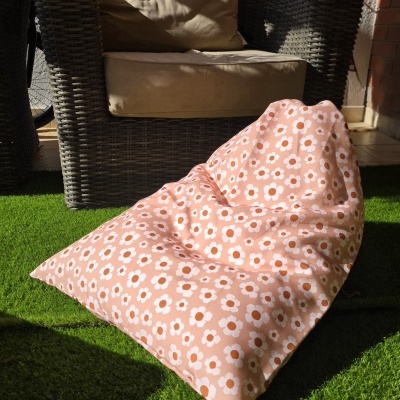 Poltrona de exterior preta com almofadas bege e puff cor-de-rosa com flores brancas e laranjas na relva.