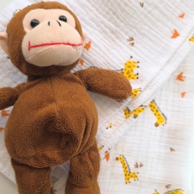 Peluche de macaco castanho sobre manta branca com padrão de girafas.