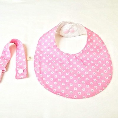 Babete rosa com padrão de flores brancas e faixa rosa para prender sobre fundo branco