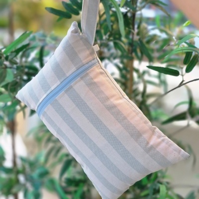 Bolsa de tecido riscada branca e cinzenta com fecho azul numa mão junto a plantas.