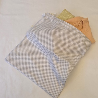 Saco de tecido cinzento com padrão de pequenas cruzes, contendo t-shirt cor de pêssego e pano verde