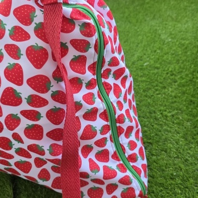 Mochila com padrão de morangos vermelhos e verdes com fecho verde em relva verde