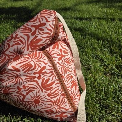 Mochila em tecido com padrão laranja e bege colocada sobre relva