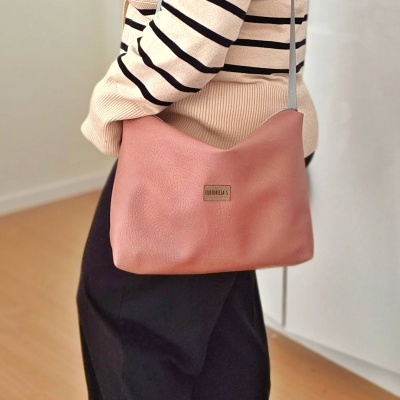 Mala rosa de ombro em ambiente interior com pessoa vestindo casaco bege riscas pretas e saia preta