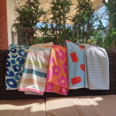 Cinco toalhas coloridas com vários padrões dobradas sobre móvel de vime castanho em ambiente exterior