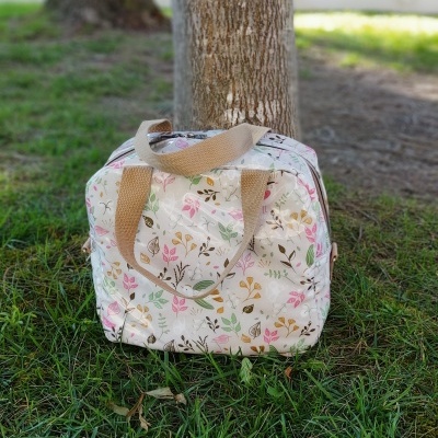 Mala quadrada de tecido com padrão floral em relva junto a árvore